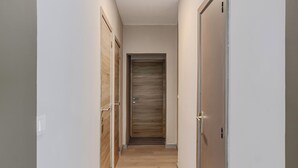Un couloir étroit, doté d’un plancher en bois et de murs blancs, qui mène à une porte au fond.