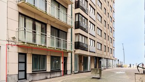 Un immeuble à plusieurs étages doté de balcons, de grandes fenêtres et d’une zone au rez-de-chaussée dallée.