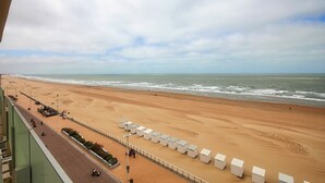 A beach with a row of white beach huts along the shore, a sandy beach, and the ocean in the background.