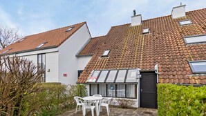 Een woongebouw met een pannendak, een kleine tuin met een tafel en stoelen, en een zwarte deur.
