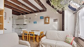 Een gezellige woonkamer met een bank, een eettafel met stoelen en een keuken op de achtergrond.