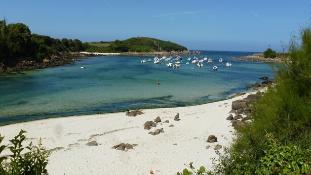 A beach with clear turquoise water, white sand, and rocky outcrops.