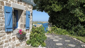 A stone building with blue shutters, a wooden deck, and a garden with a stone pathway.