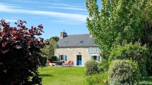 A stone house with a blue door, surrounded by lush greenery and a well-maintained lawn.