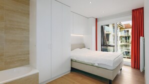 A modern bedroom with a bed, a built-in wardrobe, a glass door leading to a balcony, and a wooden floor. - 2 bedroom accommodation in Oostduinkerke (Oostduinkerke)