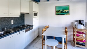Eine Küche mit weißen Schränken, einem Herd und einer Mikrowelle. An der Wand hängt ein Gemälde und es gibt einen Tisch mit Stühlen.
