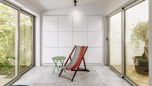 Ein modernes Zimmer mit großen Schiebeglasfenstern, einem grünen Klappstuhl und einem gestreiften Liegestuhl.