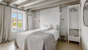 Ein Schlafzimmer mit einem Bett, einer Pendelleuchte, einem Kleiderschrank und einem Fenster mit Vorhängen.