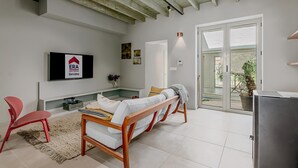 Ein modernes Wohnzimmer mit einer Couch, einem roten Sessel, einem an der Wand montierten Fernseher und einer Schiebetür zu einem Außenbereich.