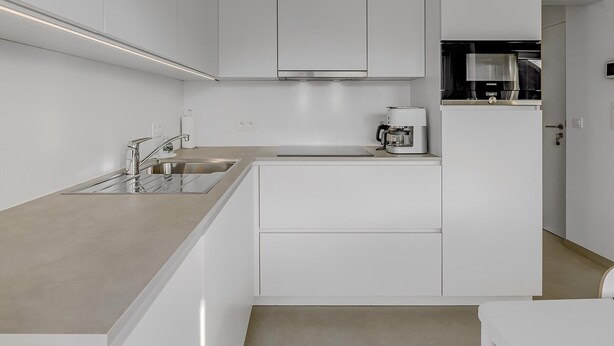 Une cuisine moderne avec des meubles blancs, un évier en acier inoxydable et une machine à café.