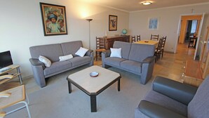 Ett vardagsrum med två grå soffor, ett soffbord och en TV-bänk. Längre bak i rummet står ett matbord med stolar.