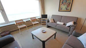Ett vardagsrum med en soffa, en fåtölj och ett soffbord. Det finns en tv på ett tv-bord och en tavla på väggen.