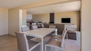 Un salon moderne avec un coin repas, une cuisine à l’arrière-plan et un téléviseur à écran plat fixé au mur.