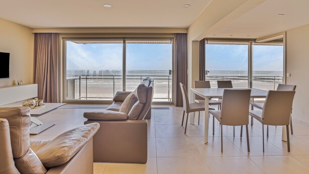 Une chambre d’hôtel moderne dotée d’une grande fenêtre donnant sur la plage et le paysage urbain.