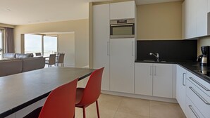 Une cuisine moderne avec des armoires blanches, un comptoir noir et un four encastré. On y trouve également un coin repas avec une table grise et des chaises rouges.