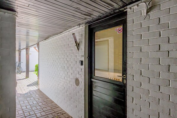 A corridor with a white brick wall, a black door with a window, and a metal ceiling.