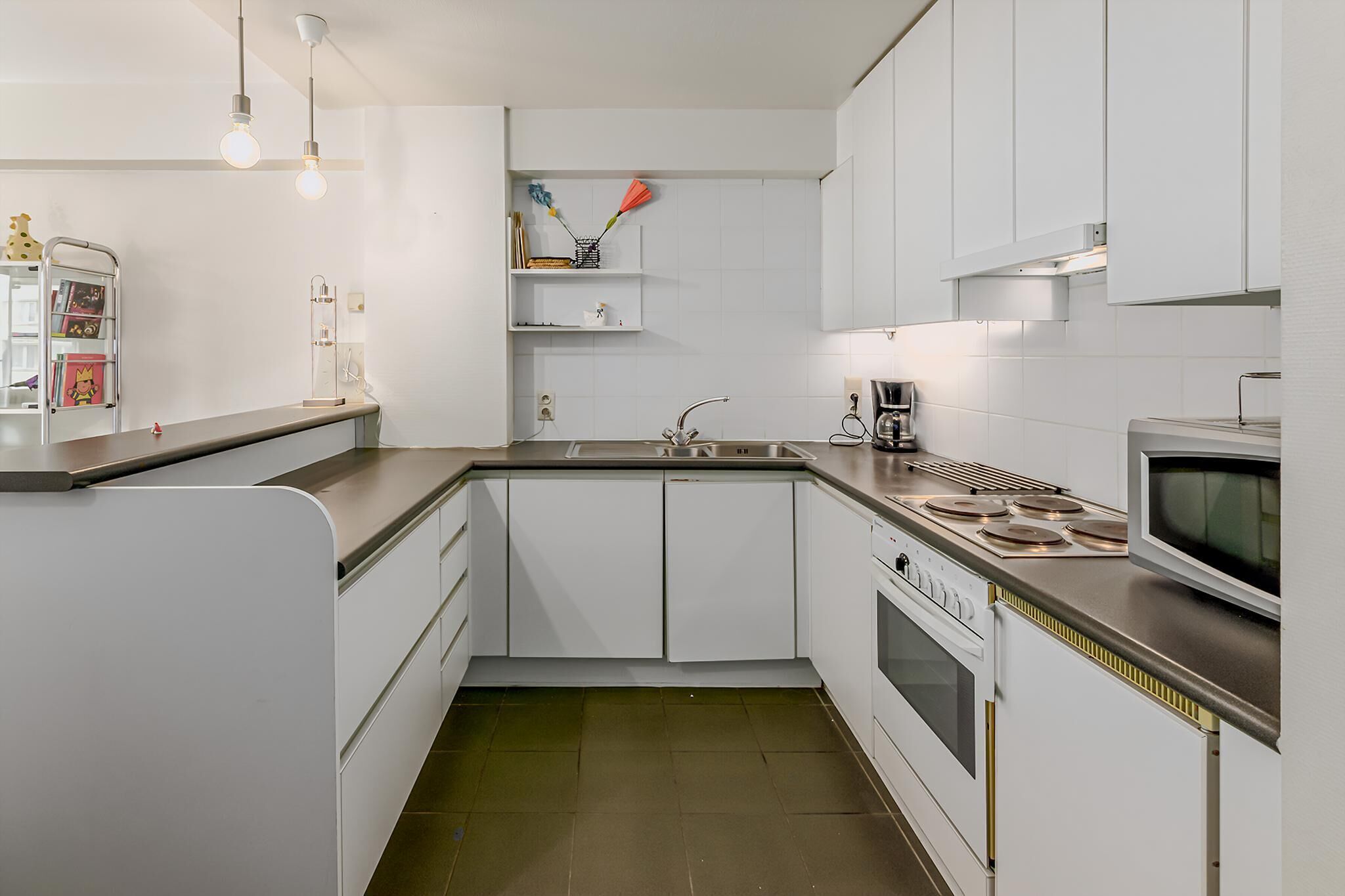 A modern kitchen with white cabinetry, a stainless steel countertop, a built-in oven, and a microwave.