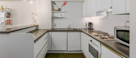 A modern kitchen with white cabinetry, a stainless steel countertop, a built-in oven, and a microwave.
