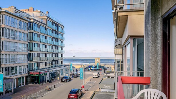 Een kuststraat met moderne gebouwen, een heldere lucht en uitzicht op zee.