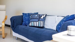 Un canapé bleu orné de coussins à motifs, une chaise en bois et une table blanche sur laquelle se trouve une tasse.