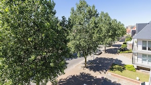 Un quartier résidentiel avec des arbres, une route goudronnée et un immeuble doté d’un balcon.