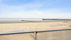 Blick auf einen Strand mit einem Steg, der ins Meer führt, einem klaren Himmel und einem Sandstrand.