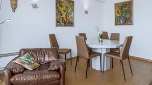 A dining area with a round table, six chairs, a brown leather sofa, and two wall-mounted paintings. - 2 bedroom accommodation in Sint Idesbald (Sint Idesbald)