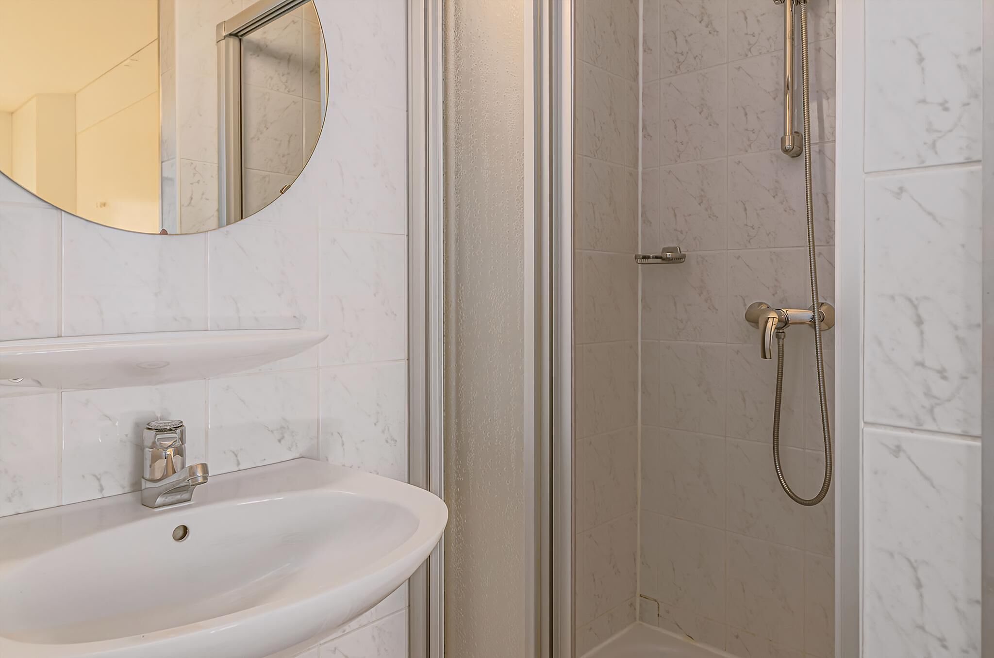 A bathroom with a sink, mirror, and shower.