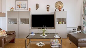 A modern living room with a large flat-screen TV, a glass coffee table, a brown leather sofa, and a bookshelf with decorative items. - 2 bedroom accommodation in Sint Idesbald (Sint Idesbald)