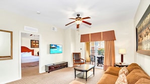 Habitación de hotel con cama, televisor, ventilador de techo, sofá, mesa de centro y balcón con vistas.