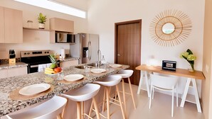 Een moderne keuken met granieten aanrechtbladen, witte barkrukken, een eettafel en een inbouwoven.