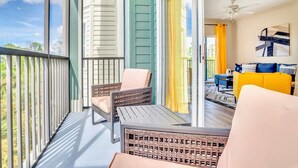 A balcony with wicker furniture, a sliding glass door leading to a living room with a yellow sofa and a ceiling fan. - 3BR Condo - Pool Hot Tub Sauna - Near Disney (Winter Garden)