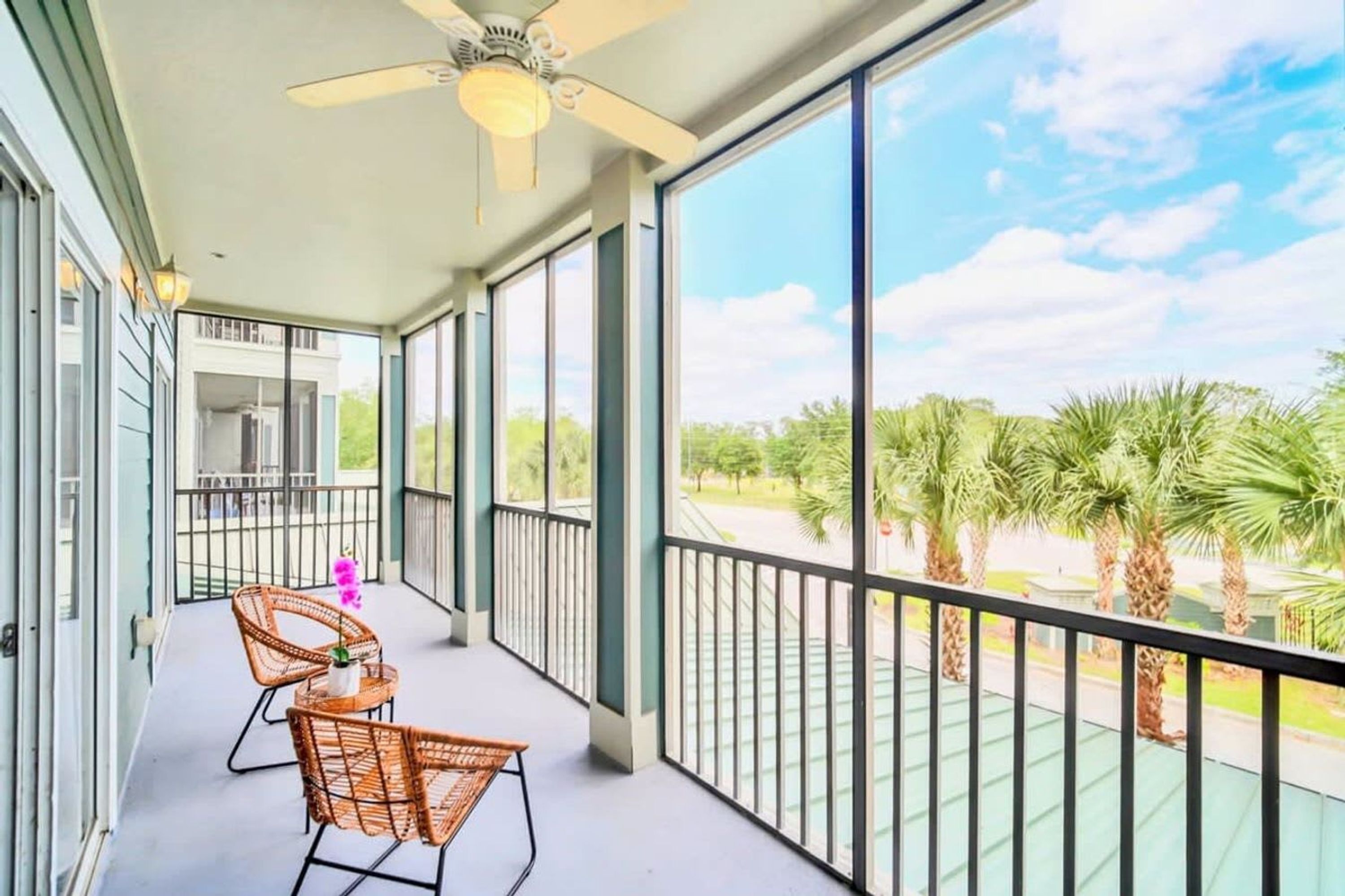Un balcon avec des fauteuils en osier, une petite table et un ventilateur de plafond.
