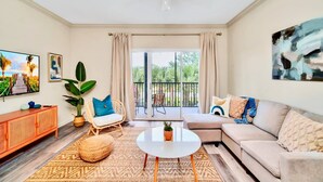 Un salon comprenant un canapé, une table basse, un téléviseur et un balcon donnant sur un espace verdoyant.