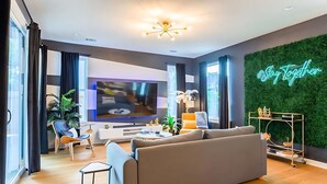 Ein modernes Wohnzimmer mit einem großen Flachbildfernseher, einem grauen Sofa, einem Couchtisch und einer Zierpflanze.