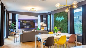 Ein modernes Wohnzimmer mit einer Couch, einem Esstisch, Stühlen, einem Flachbildfernseher und einer grünen Wand mit einem Neonzeichen.