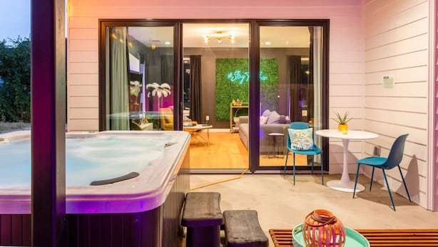 Ein moderner Außenbereich mit Whirlpool, Sitzgelegenheiten und einer Glastür zu einem Innenraum.