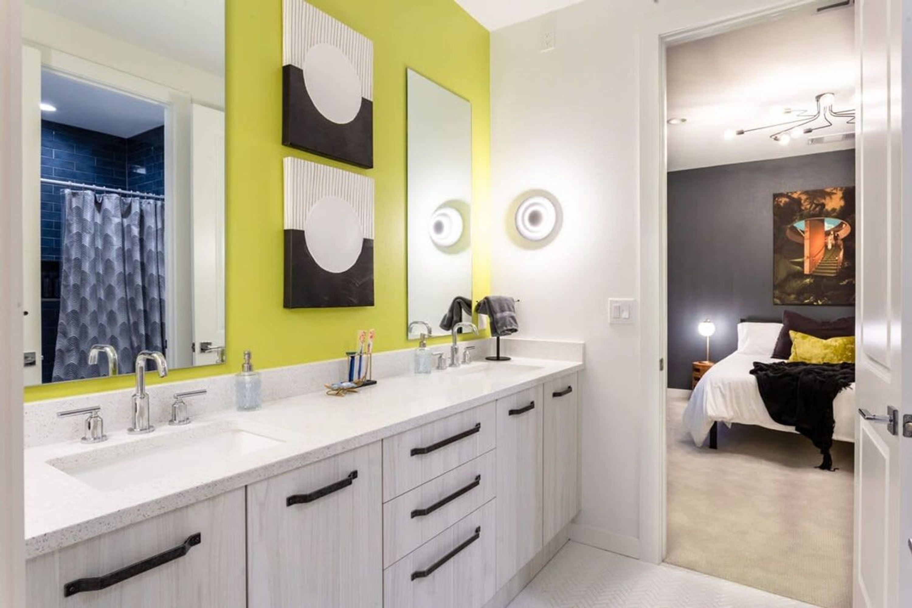 Un baño moderno con un lavamanos blanco, dos espejos y una pared de acento verde.