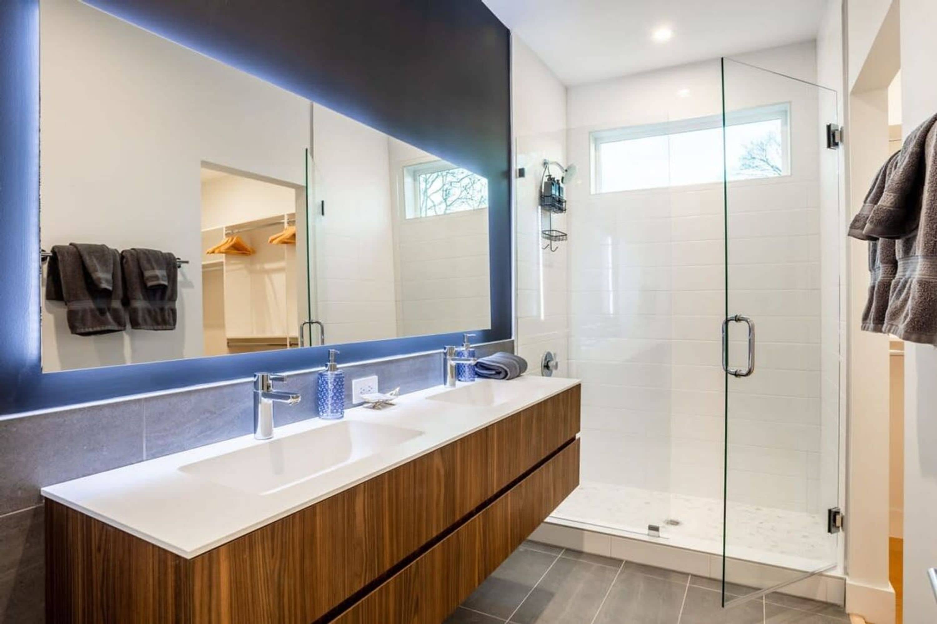 Een moderne badkamer met een houten wastafelmeubel, een grote spiegel en een douche met glazen wanden.