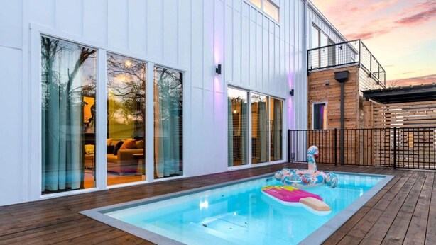 Une maison moderne dotée d’une piscine, de grandes fenêtres et d’une terrasse en bois.