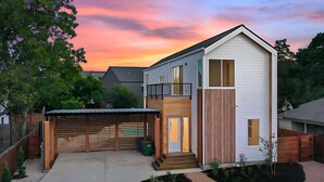 Une maison moderne à deux étages, dotée d’un patio couvert, d’une clôture en bois et d’un jardin bien entretenu.