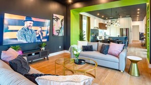 Un salon moderne doté d’un grand téléviseur à écran plat, d’un canapé, d’une table basse et d’un coin repas visible à travers une porte ouverte.