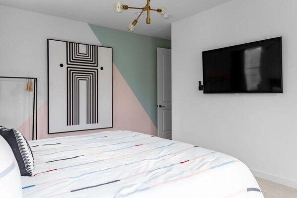 Une chambre à coucher moderne avec un lit, un téléviseur et une œuvre d’art géométrique accrochée au mur.