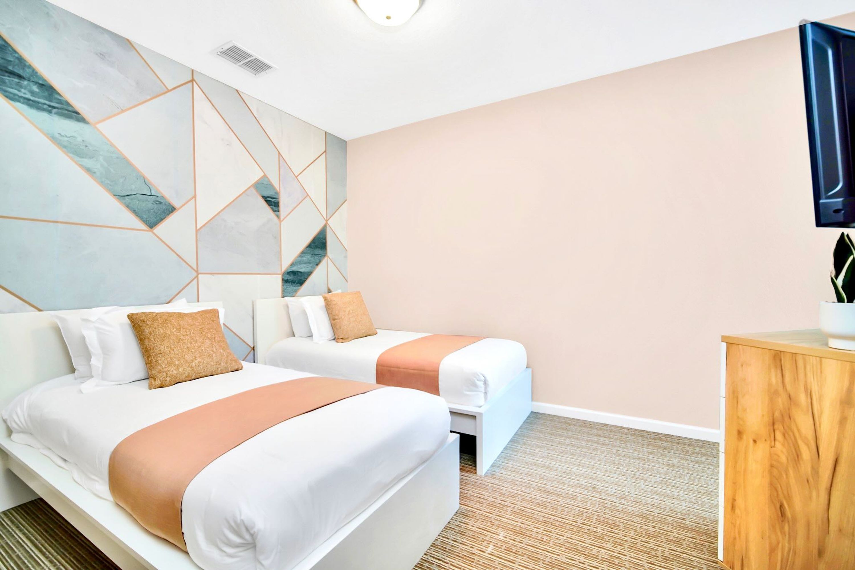 A hotel room with two beds, a wooden cabinet, and a wall with geometric patterns.
