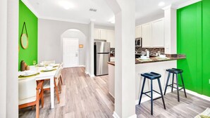 A modern kitchen with white cabinets, a stainless steel refrigerator, and a green accent wall.
