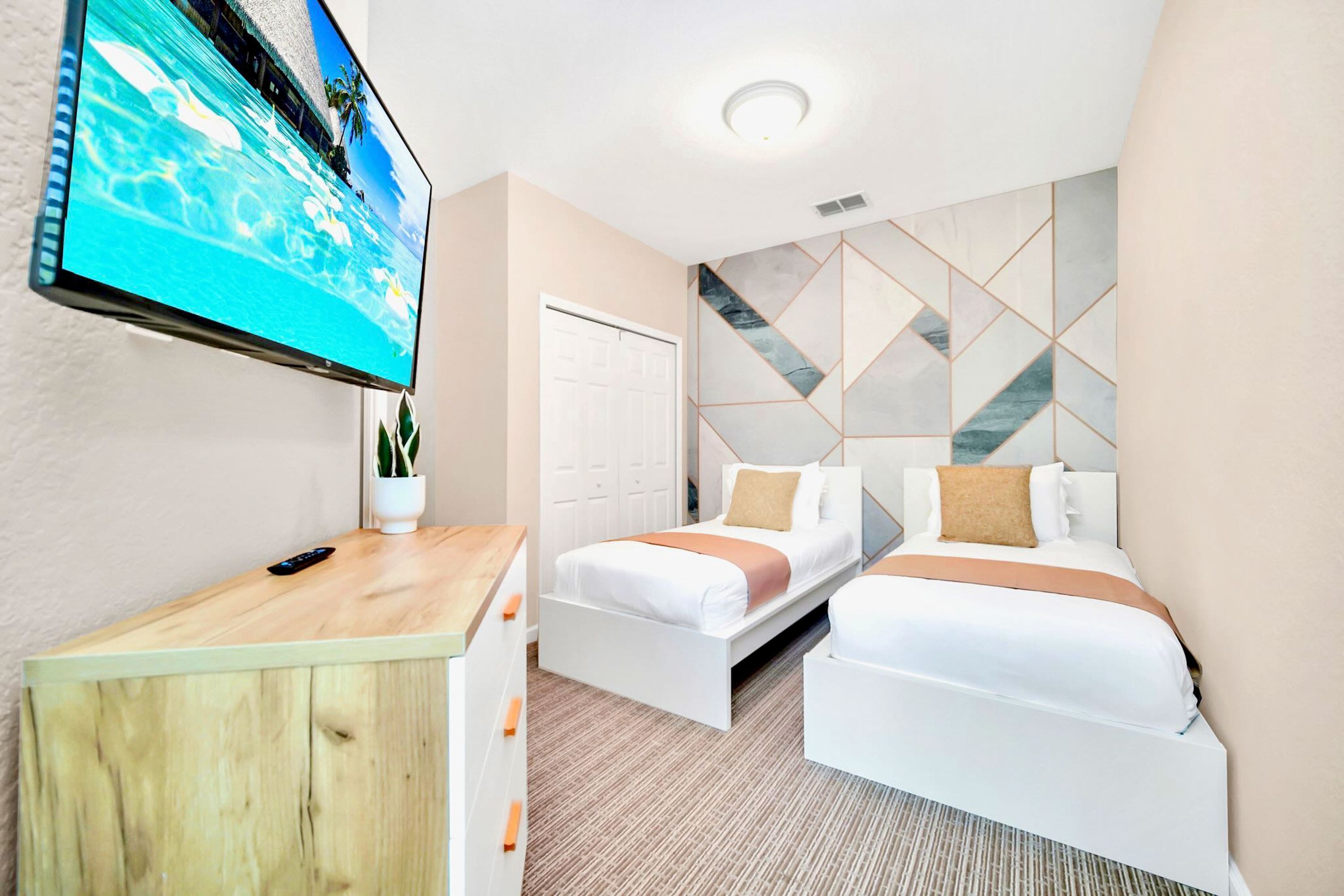 Habitación de hotel con dos camas, un televisor en la pared, un escritorio de madera y un diseño geométrico en la pared.