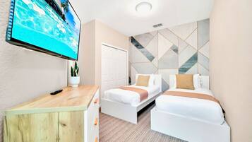 Habitación de hotel con dos camas, un televisor en la pared, un escritorio de madera y un diseño geométrico en la pared.