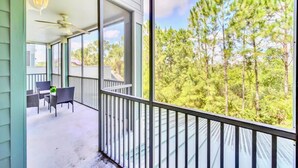 A balcony with a view of a forest, a table with chairs, and a ceiling fan.