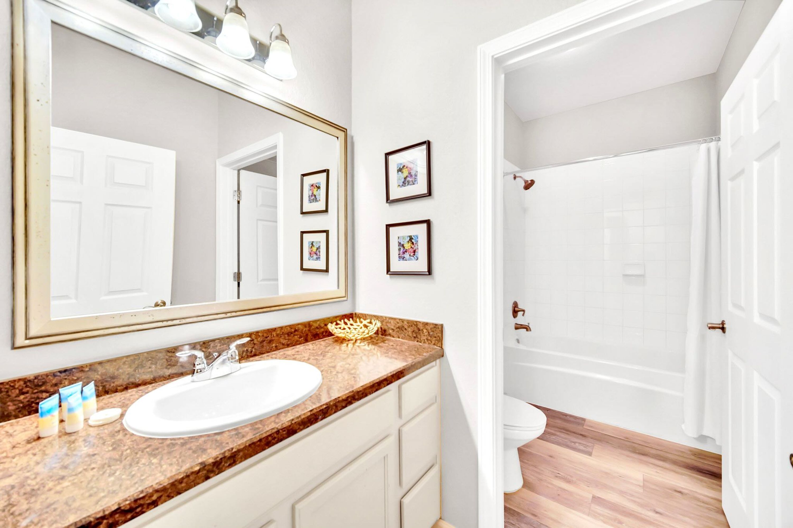 A bathroom with a large mirror, a sink with a marble countertop, and a shower area.
