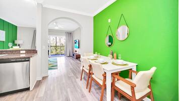 A modern kitchen with a dishwasher, a dining area with a white table and chairs, and a bright green accent wall with two round mirrors.